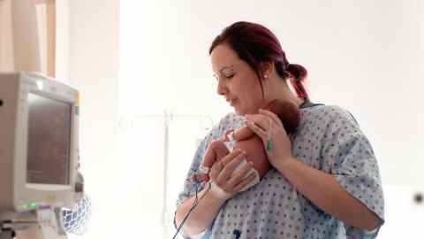 Mum cuddles preterm baby attached to monitor and tubes