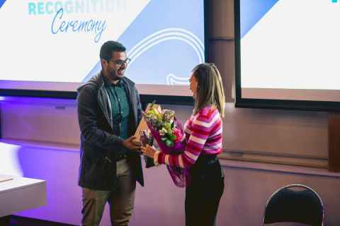 Two people at an awards ceremony. One is receiving flowers from the other.