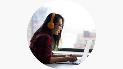 Woman wearing headphones sitting in from of an open laptop screen