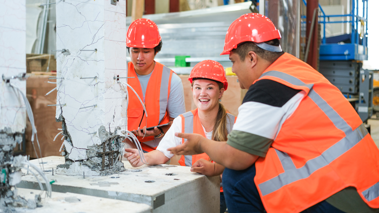 Three students in high vis gear looking at a building structure.