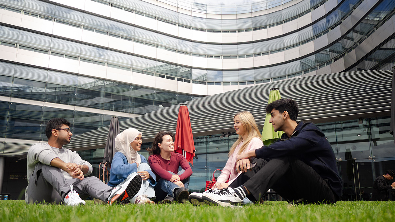 Group of students sitting on the grass outside the Business School.