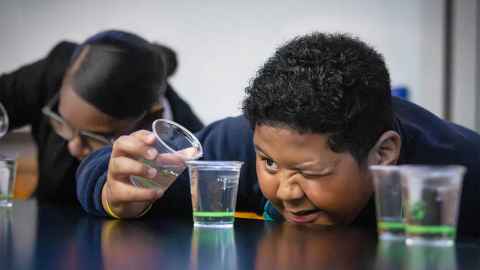 School student pouring liquid between plastic cups