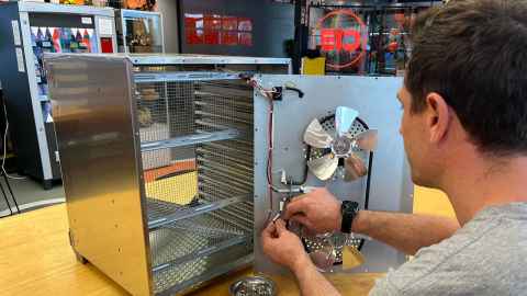  A man repairing the electrical wiring on a fan housed inside a metal box