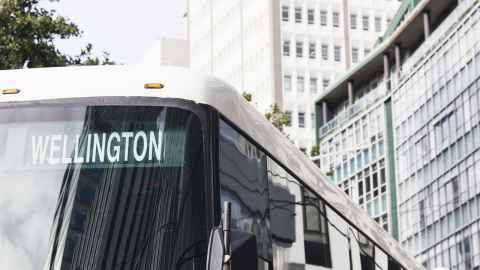 The top of a bus with a Wellington sign in the window. High-rise buildings are in the background
