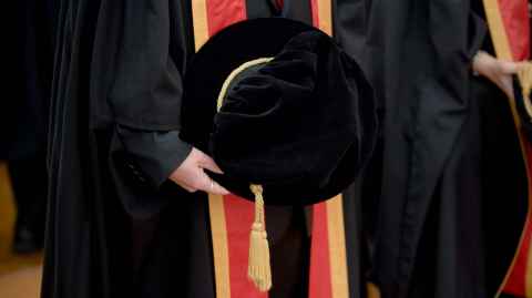 Doctoral candidate wearing gown and hand holding a doctoral cap.