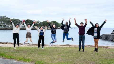 Smiling students jumping in the air by the beach.
