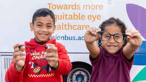 Two children stand outside the vision bus holding glasses