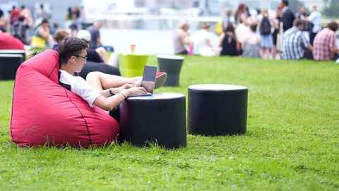 Students seated outside in a red beanbag working on a laptop.