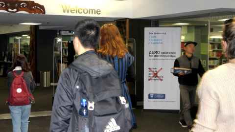students walking past a zero tolerance for discrimination sign