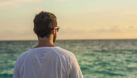 Man standing on beach looking wistfully out to sea