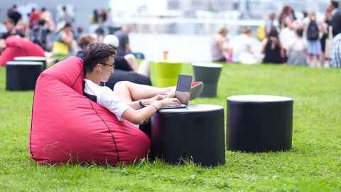 Person using a laptop while sitting on a beanbag outdoors