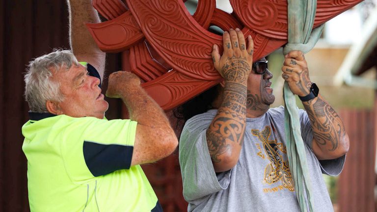 Master carver Arekatera (Katz) Maihi, Ngāti Whātua Ōrākei and Ngāpuhi, with Keith Walker, builder of Tāne-nui-a-rangi in 1987, together positioning the new maihi on Tāne-nui-a-rangi in 2024.