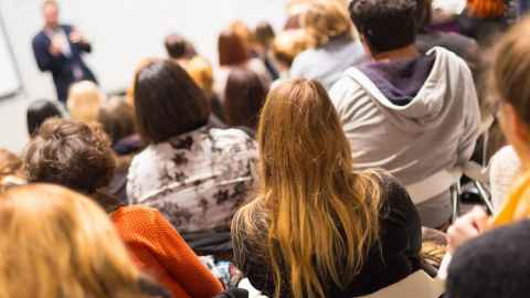 Students in lecture theatre from behind looking towards lecturer at the front.