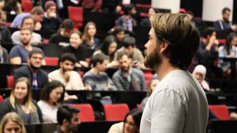Lecturer at the front of a lecture theatre speaking to students