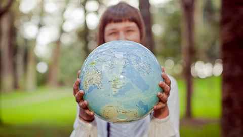 A child standing in front of trees, holding a globe in her hands with New Zealand facing the viewer