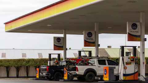Two utes, one black, one white, in adjacent bays, refuelling at a Z gas station. The black ute has two dirt bikes loaded in the boot area. 