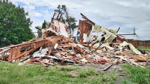 The remains of a destroyed house, including wood, are piled onto a patch of grass and concrete