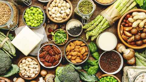 A set of plant-based vegetarian food sources clustered on a table. Includes legumes, beans, lentils, vegetables, nuts and seeds. 