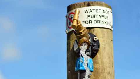 An outdoor tap fixed to a wooden post beneath a sign saying water not suitable for drinking