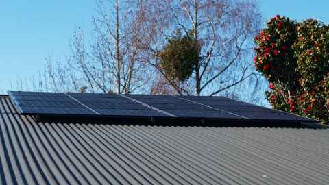 Eight solar panels on the roof of a home. Trees are in the background against a blue sky.