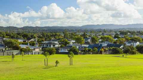 In the foreground is green parkland with a smattering of newly planted trees. Behind that is a suburban area with residential housing. In the background are forrested hills.Photo: iStock.