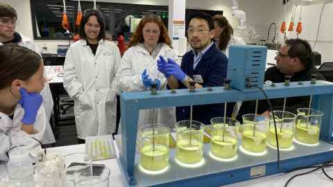 A researcher in a lab, surrounded by a small group of observers.
