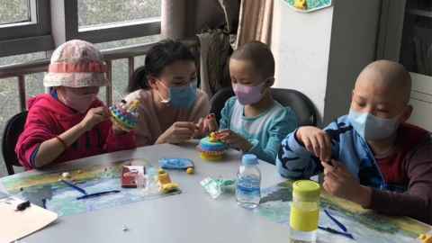 A woman helping three children with an activity.