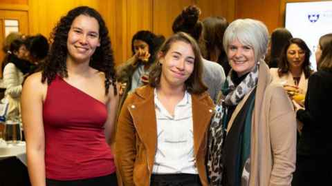 Two young women with one older woman at a gathering of people.