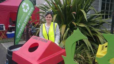 A young woman surrounded by bins, next to a sign reading, "Towards zero waste".