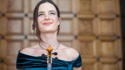 A smiling young woman in an evening gown, holding a violin.