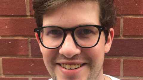 A young man wearing glasses, smiling.