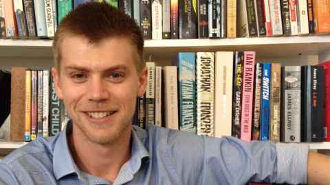A smiling young man in front of bookshelves.