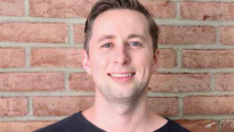 A man standing in front of a brick wall, smiling.