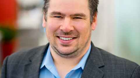 A smiling man in a blue shirt and suit jacket.