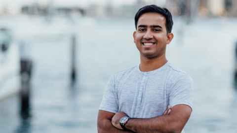 A young man in a grey shirt standing by water.
