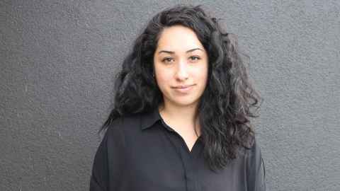 A woman with long, curly black hair, wearing a black shirt.
