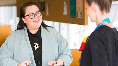 A dark-haired woman wearing glasses, in conversation with another woman.