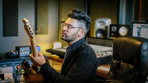A young man in a recording studio, holding a guitar.