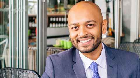 A smiling man in a dark blue suit, sitting in a cafe.