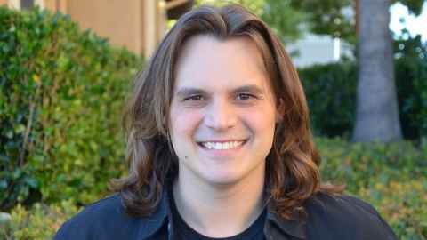 A smiling young man with long brown hair.