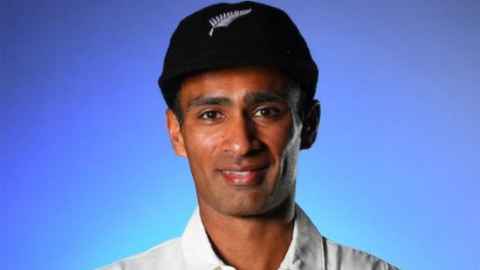 A man wearing a black hat with a silver fern on it.