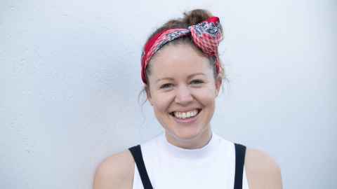 A smiling young woman wearing a multi-coloured bandanna tied around her head.
