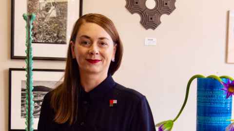 A brown-haired woman in front of a wall covered in art.