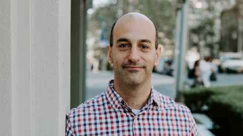 A man in a checked shirt, standing on the footpath of a city street.