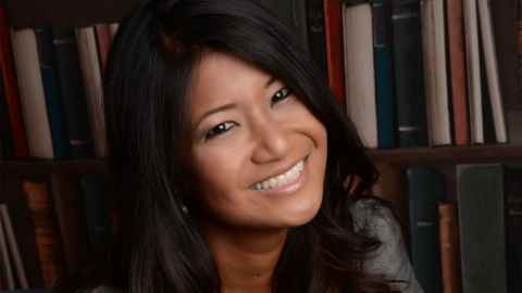 A dark-haired woman in front of shelves full of books.