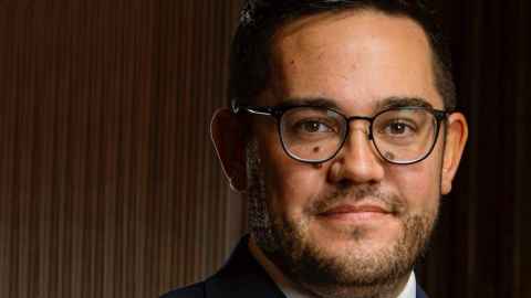 A man with glasses, wearing a black jacket and white shirt.