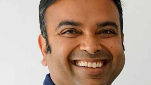 A close-up of a smiling man wearing a blue shirt.