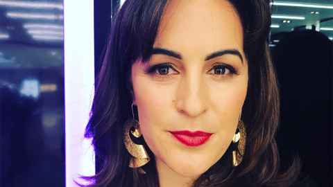 A dark-haired woman wearing bright lipstick and gold earrings.