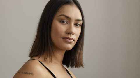 A woman with dark shoulder-length hair and a tattoo on her arm with the words 'til infinity' visible.