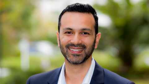 A smiling man wearing a dark blue suit jacket and white shirt.